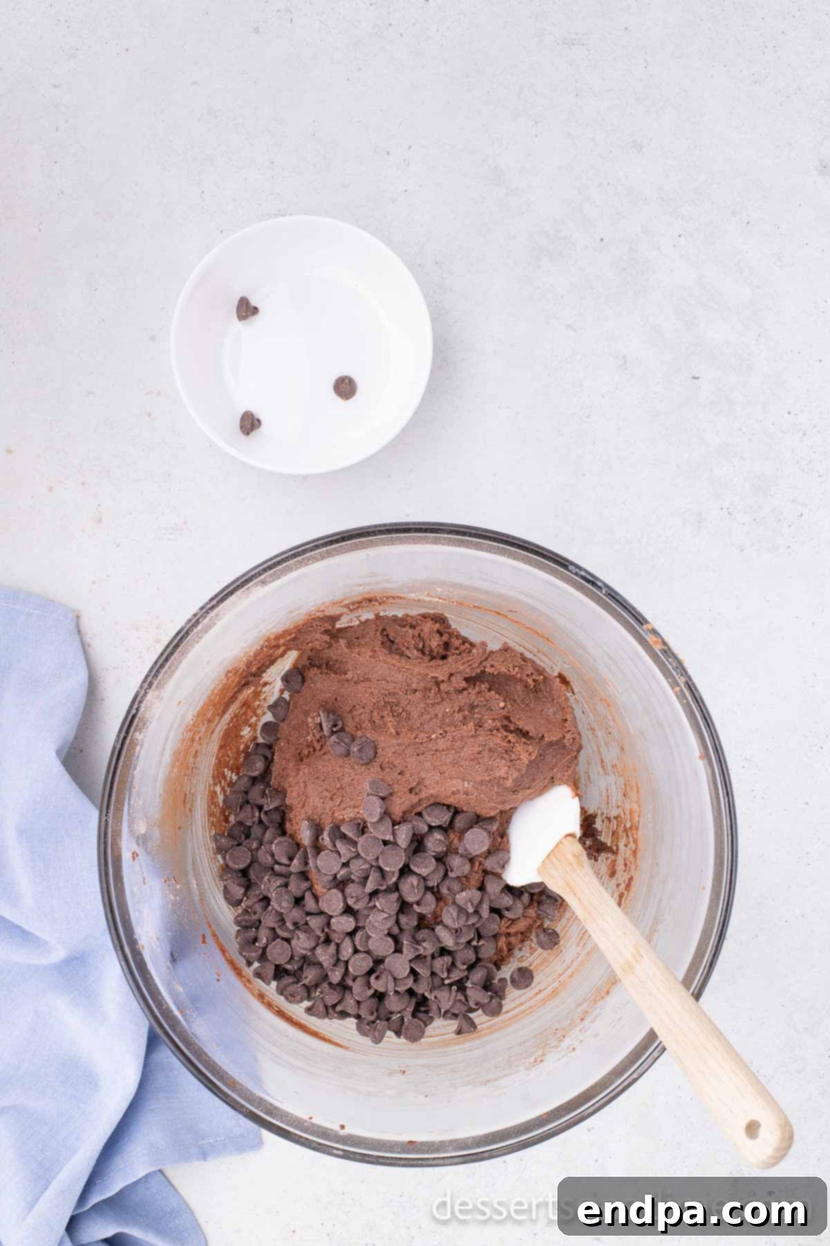 Chocolate chips gently folded into the Nutella cookie dough in a mixing bowl, preparing it for refrigeration.