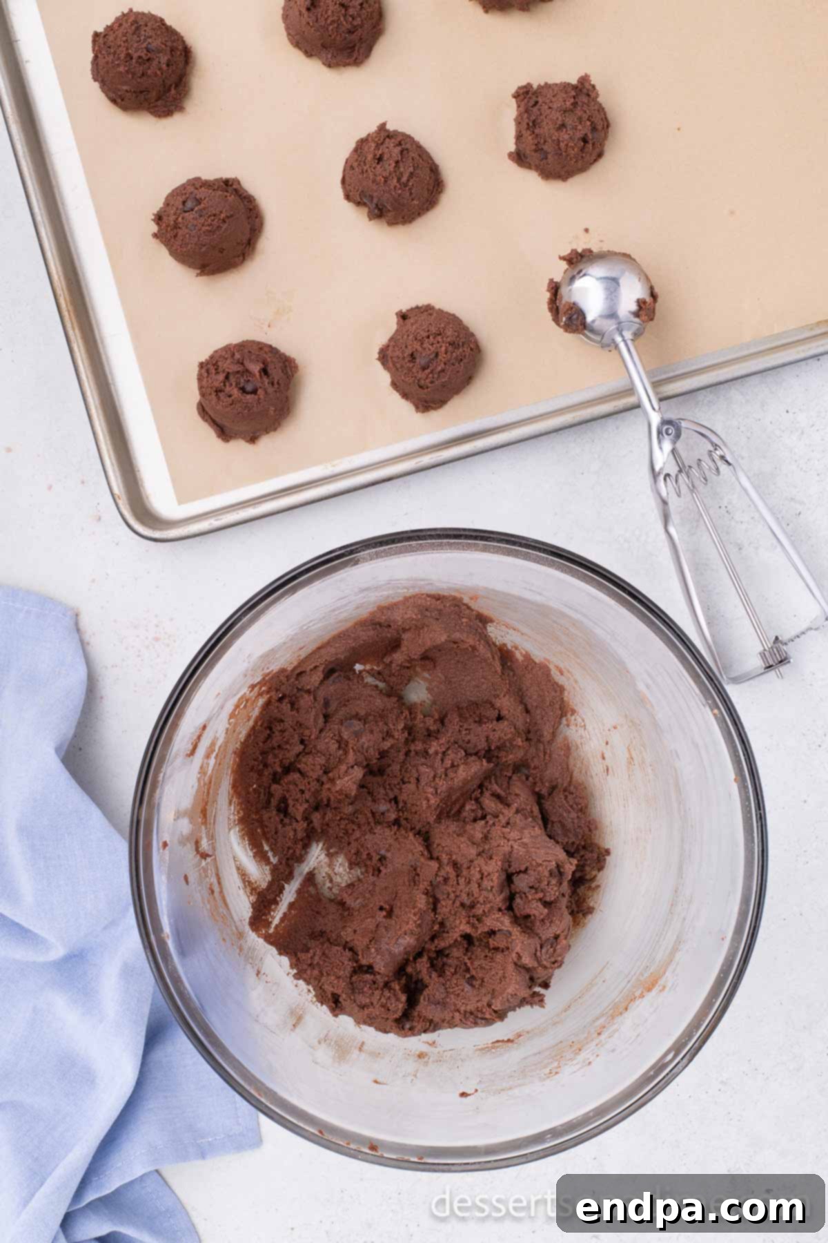 A hand using a cookie scoop to portion out Nutella cookie dough onto a baking sheet, preparing for baking.