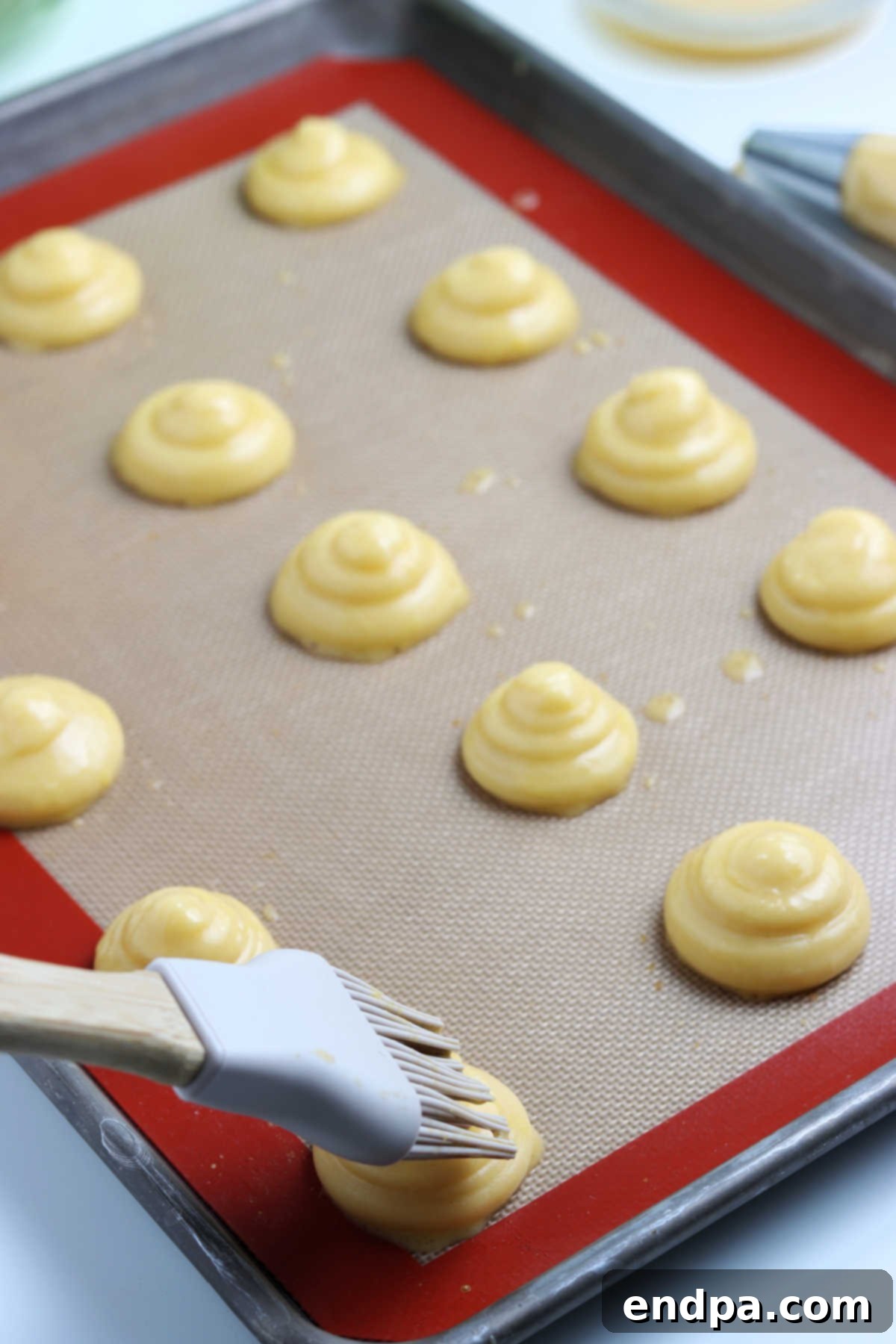 Irresistible Cream Puffs 5 Egg wash being brushed onto each piped cream puff, preparing them for baking.