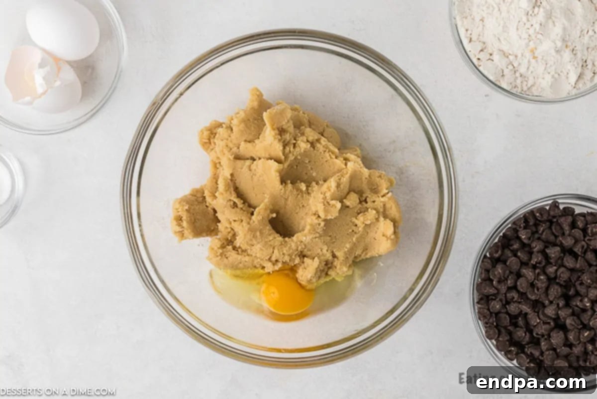 Two eggs being added to the creamed butter and sugar mixture in a large mixing bowl.