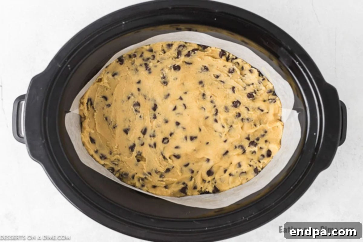 Half of the cookie dough spread in a greased slow cooker, with caramel sauce drizzled on top.