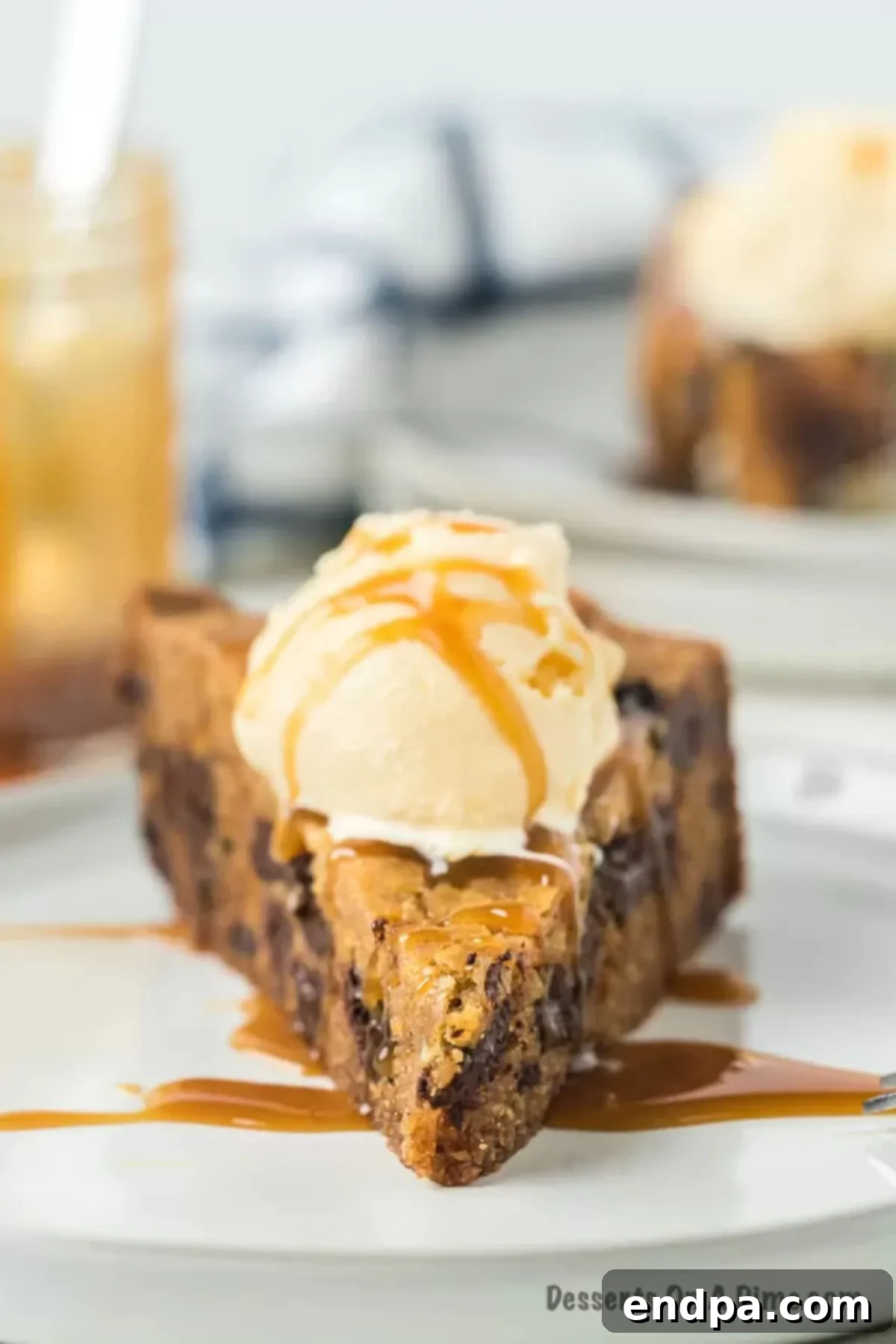A slice of slow cooker chocolate chip cookie cake topped with melting ice cream and caramel drizzle on a white plate.