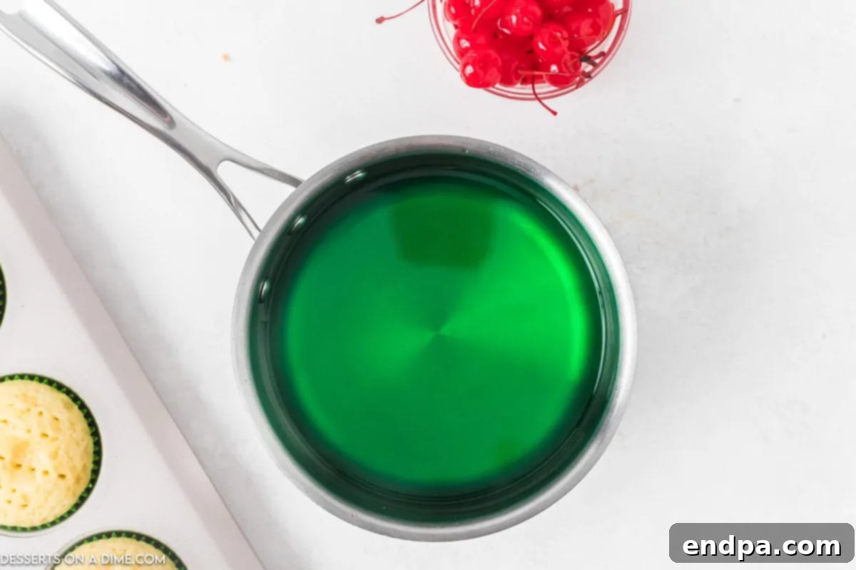 Zingy Cherry Limeade Cupcakes 5 A small saucepan containing a vibrant green jello mixture, smooth and completely dissolved in recently boiled water, off the heat.