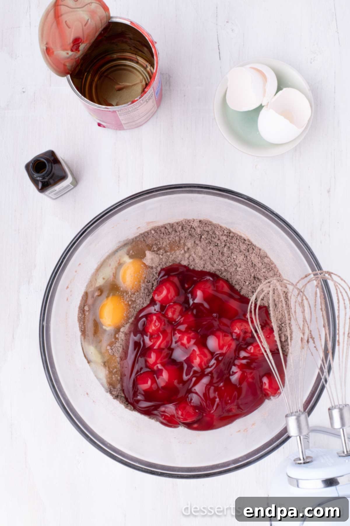 Decadent Chocolate Cherry Delight 2 A large mixing bowl containing a dark cake mix and a spoonful of cherry pie filling, with other ingredients waiting to be combined for the chocolate cherry cake.