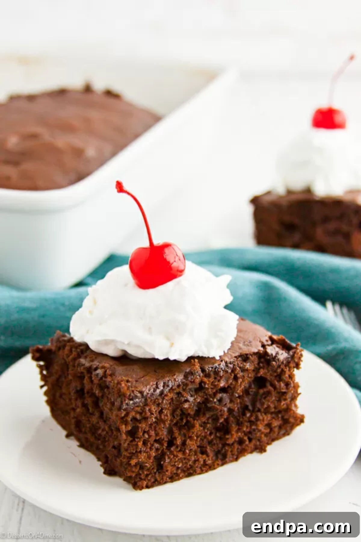 Chocolate Cherry Cake Recipe only calls for 4 simple ingredients making it super easy to enjoy dessert any day of the week. Try this chocolate cherry cake. A second close-up view of a slice of Chocolate Cherry Cake, adorned with a swirl of whipped cream and a cherry, highlighting the moist texture and cherry pieces within.