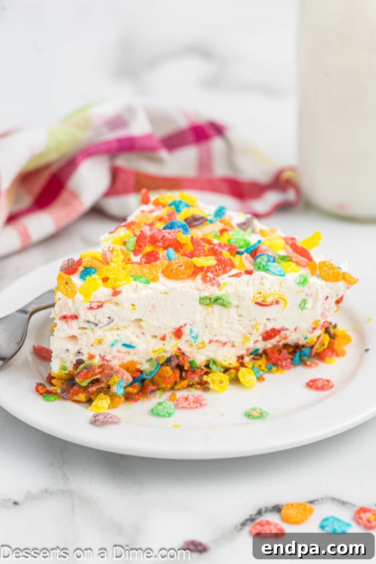 Vibrant Fruity Pebbles Cheesecake 2 A vibrant slice of Fruity Pebbles Cheesecake on a pristine white plate, showcasing its colorful cereal crust and creamy filling.