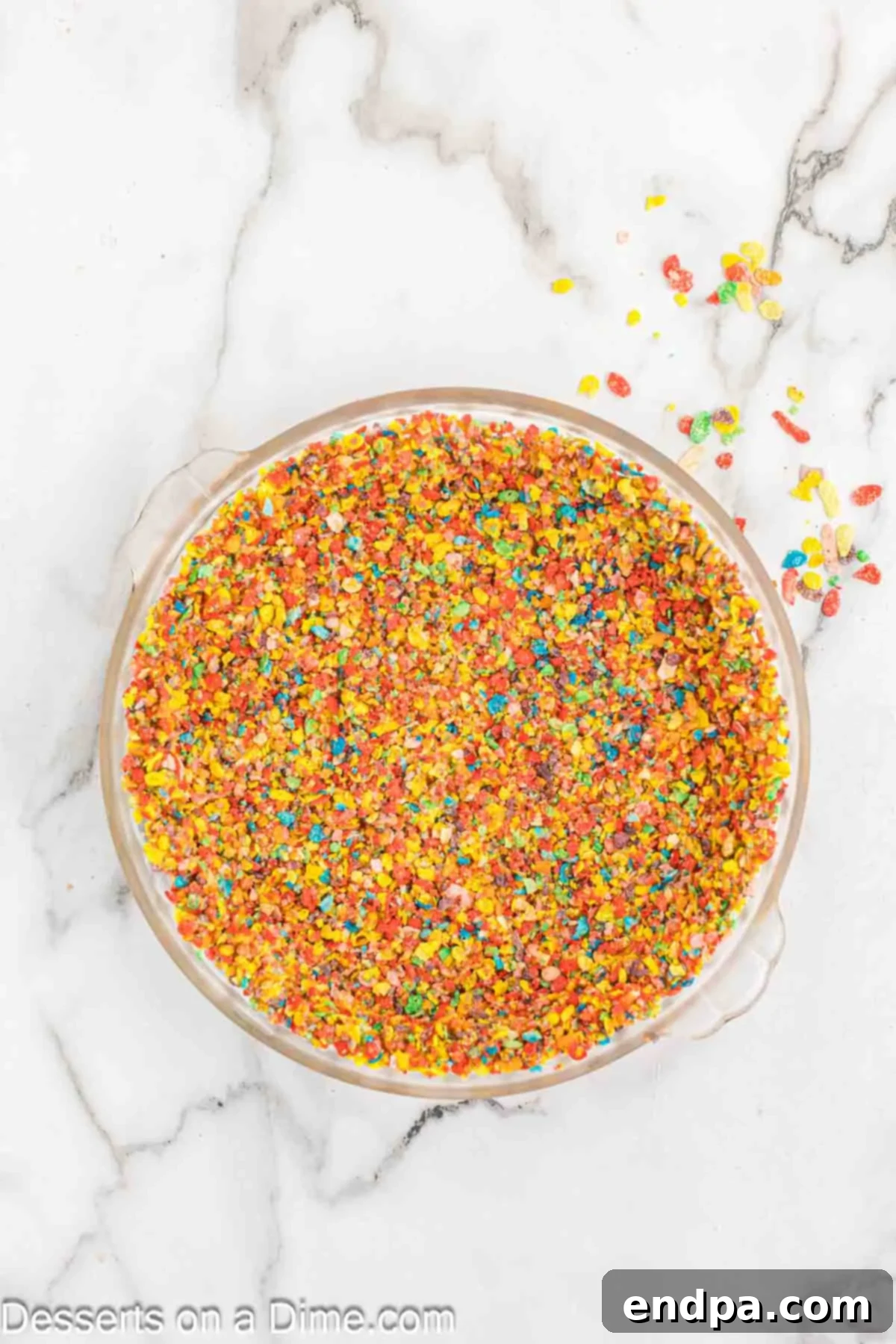 Vibrant Fruity Pebbles Cheesecake 5 Crushed Fruity Pebbles cereal mixed with melted butter and pressed firmly into a pie pan, extending slightly up the sides to form the cheesecake crust.