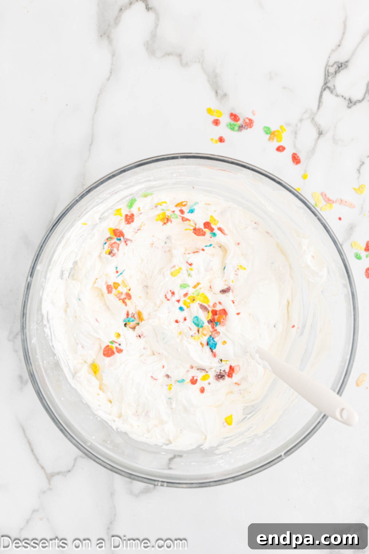 Vibrant Fruity Pebbles Cheesecake 7 Cool Whip and Fruity Pebbles cereal being gently folded into the smooth cream cheese mixture in a bowl.