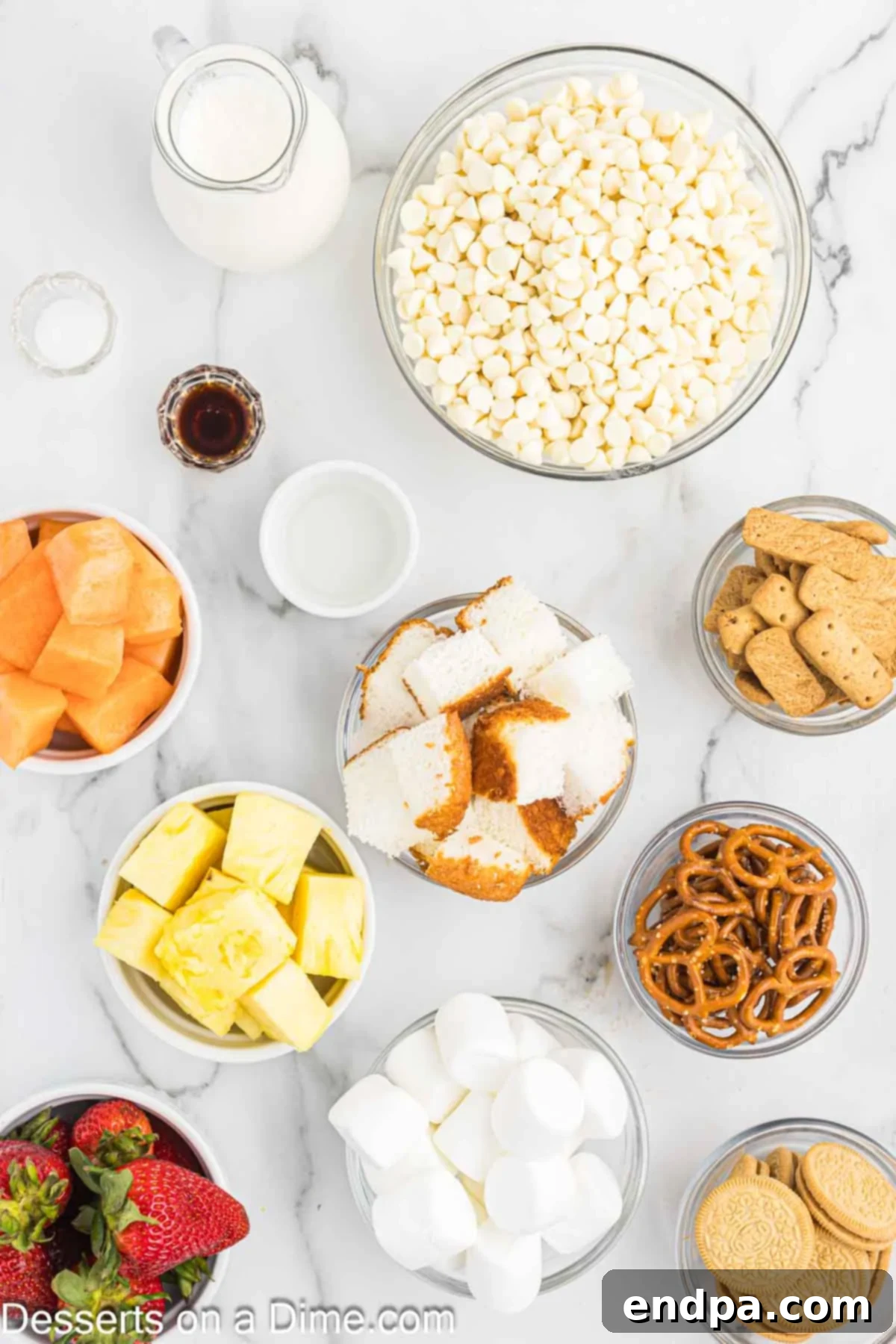 Decadent White Chocolate Fondue 3 A vibrant flat lay showcasing the key ingredients for white chocolate fondue: white chocolate chips, heavy cream, coconut oil, and vanilla extract, with an assortment of fresh dippers like fruit and pretzels.