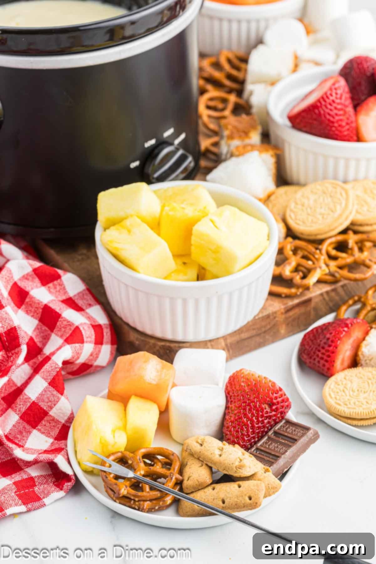 Decadent White Chocolate Fondue 6 A colorful assortment of dippers for white chocolate fondue arranged neatly on a platter, including strawberries, apple slices, marshmallows, and pretzel sticks.