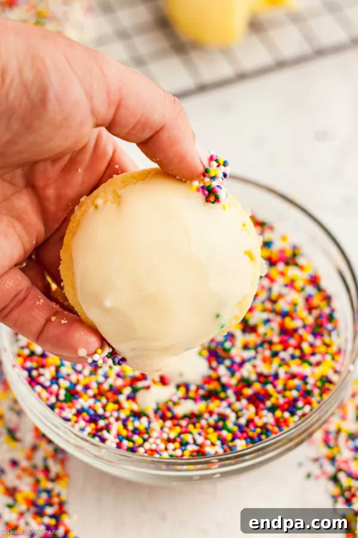 A freshly baked Italian cookie being carefully dipped and coated in a smooth, white glaze.