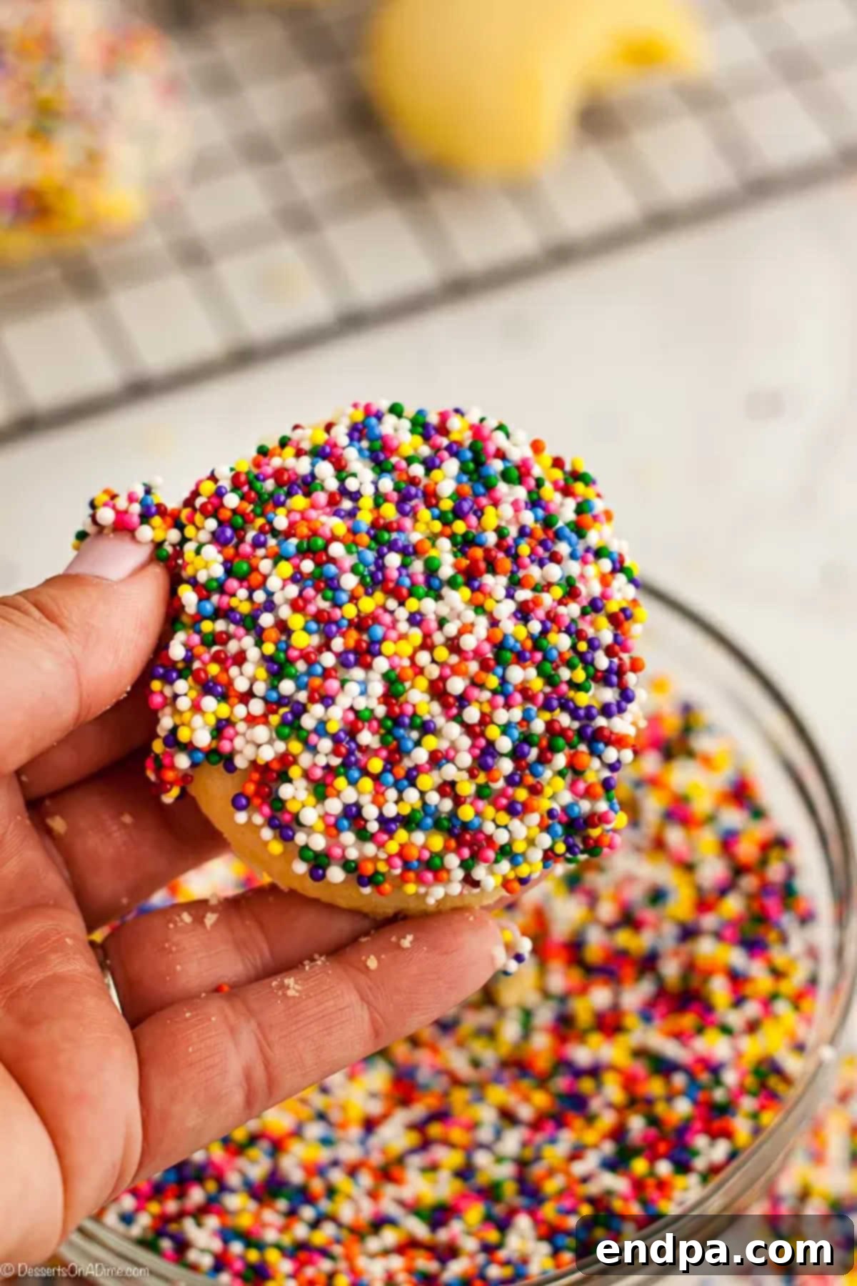 A freshly glazed Italian cookie being adorned with a generous sprinkle of colorful decorations.