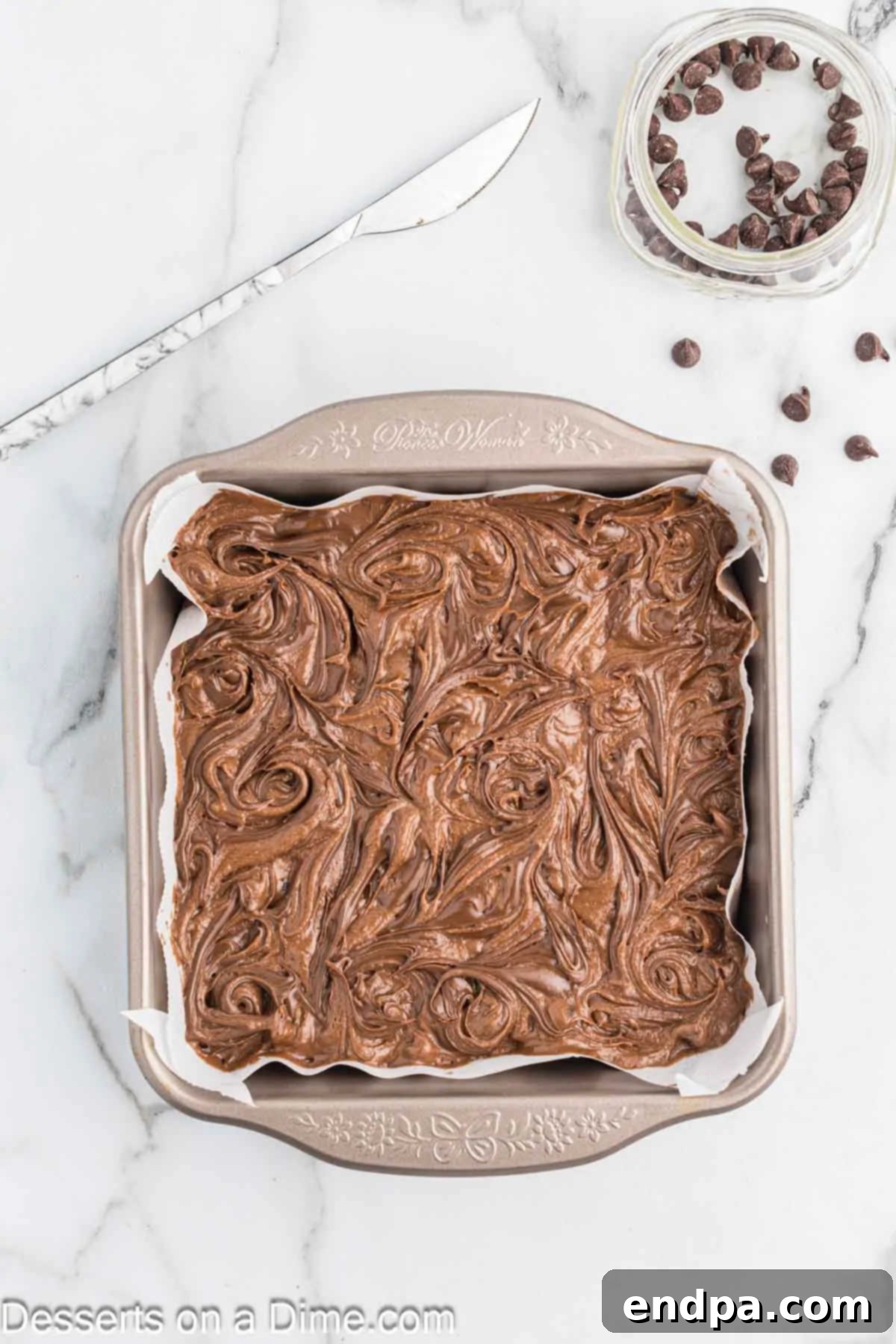 A butter knife expertly swirling Nutella into the brownie batter for a beautiful marble effect.
