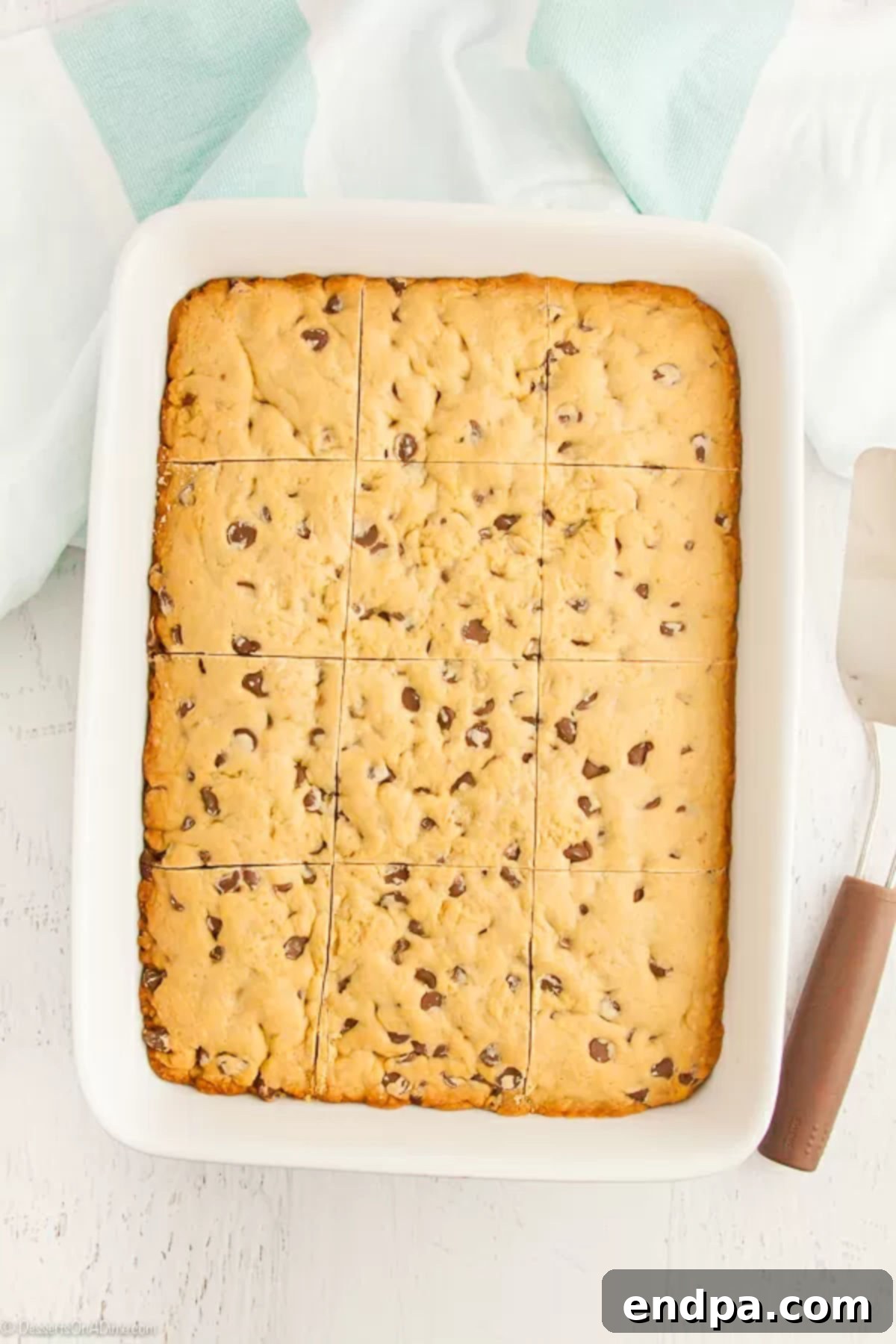 A baked chocolate chip cookie cake, already cut into even square slices within the baking pan, ready for serving.