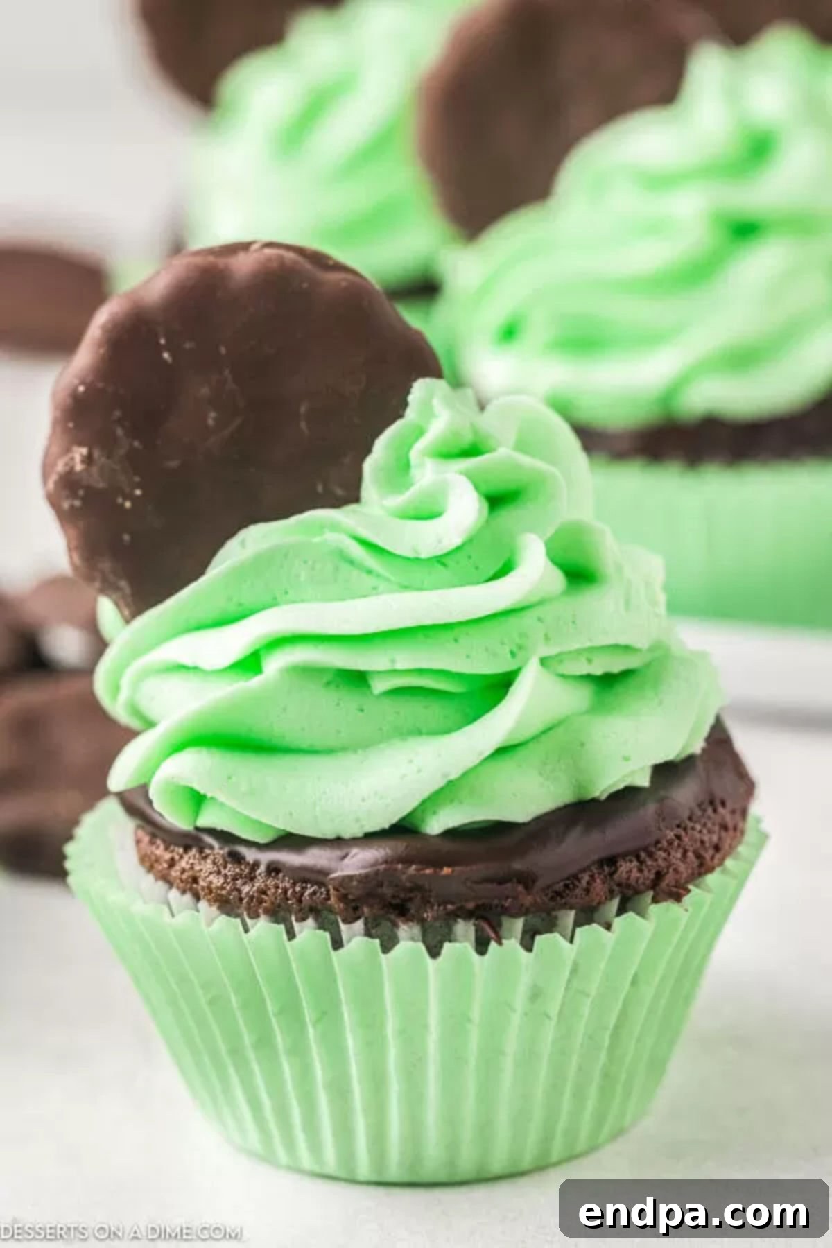 Rich and decadent Thin Mint Cupcakes topped with green mint icing and a whole Thin Mint cookie, set against a festive backdrop.