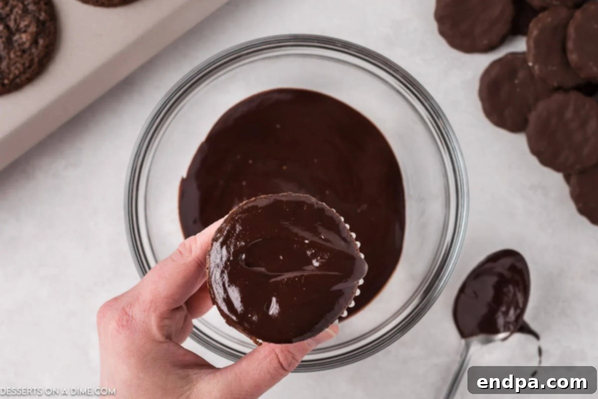 A chocolate cupcake being dipped into a bowl of smooth, glossy chocolate ganache.