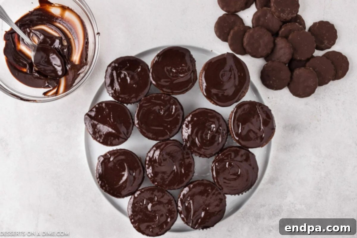 Freshly dipped chocolate ganache cupcakes arranged on a platter, allowing the ganache to set before frosting.