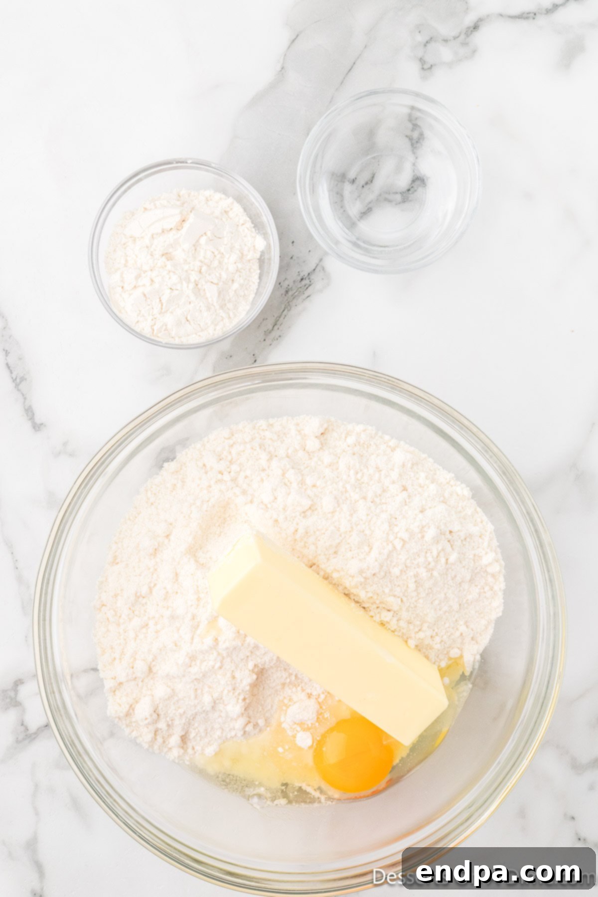 A mixing bowl containing sugar cookie mix, softened butter, and a large egg, ready to be combined into dough.