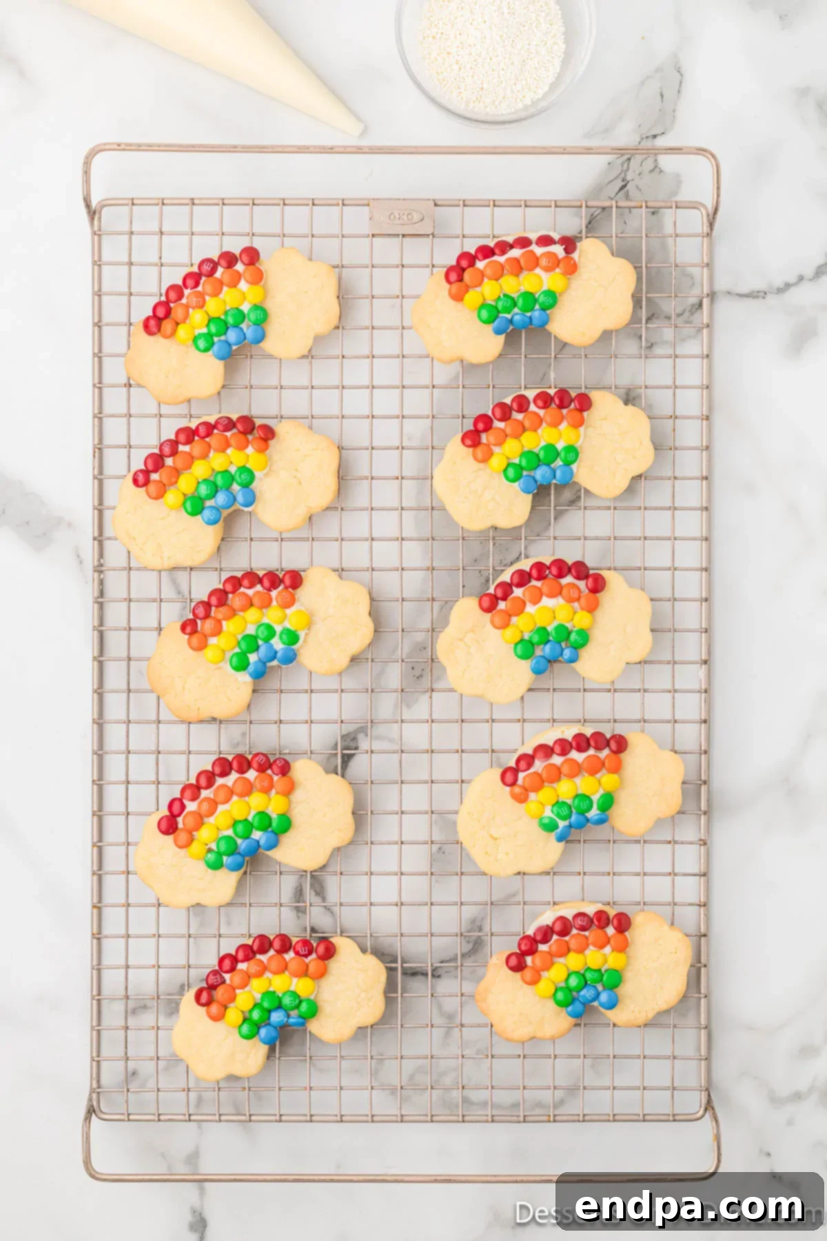 Rainbow cookies partially frosted, with miniature M&Ms arranged on the rainbow arch, illustrating the decorating process.