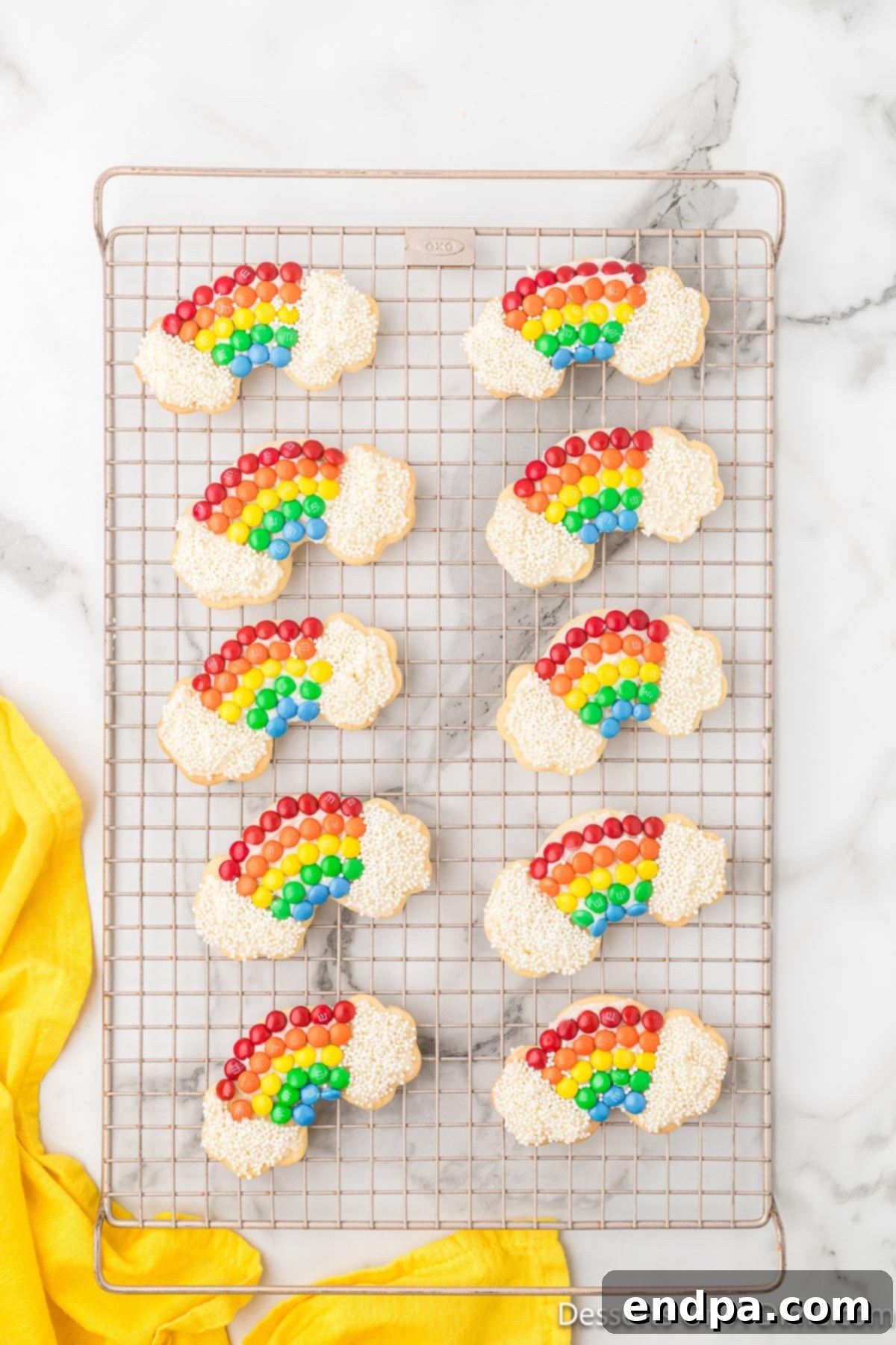 Decorated rainbow cookies showing the frosted 'clouds' topped with white sprinkles, completing the whimsical design.