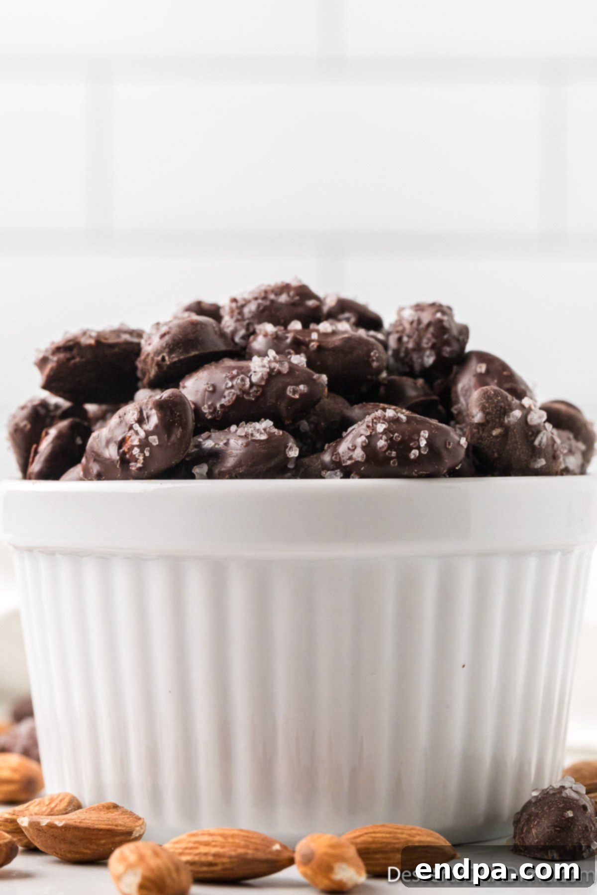 Decadent Dark Chocolate Almonds 2 A bowl filled with freshly made dark chocolate covered almonds, lightly sprinkled with sea salt, showcasing their glossy chocolate coating.