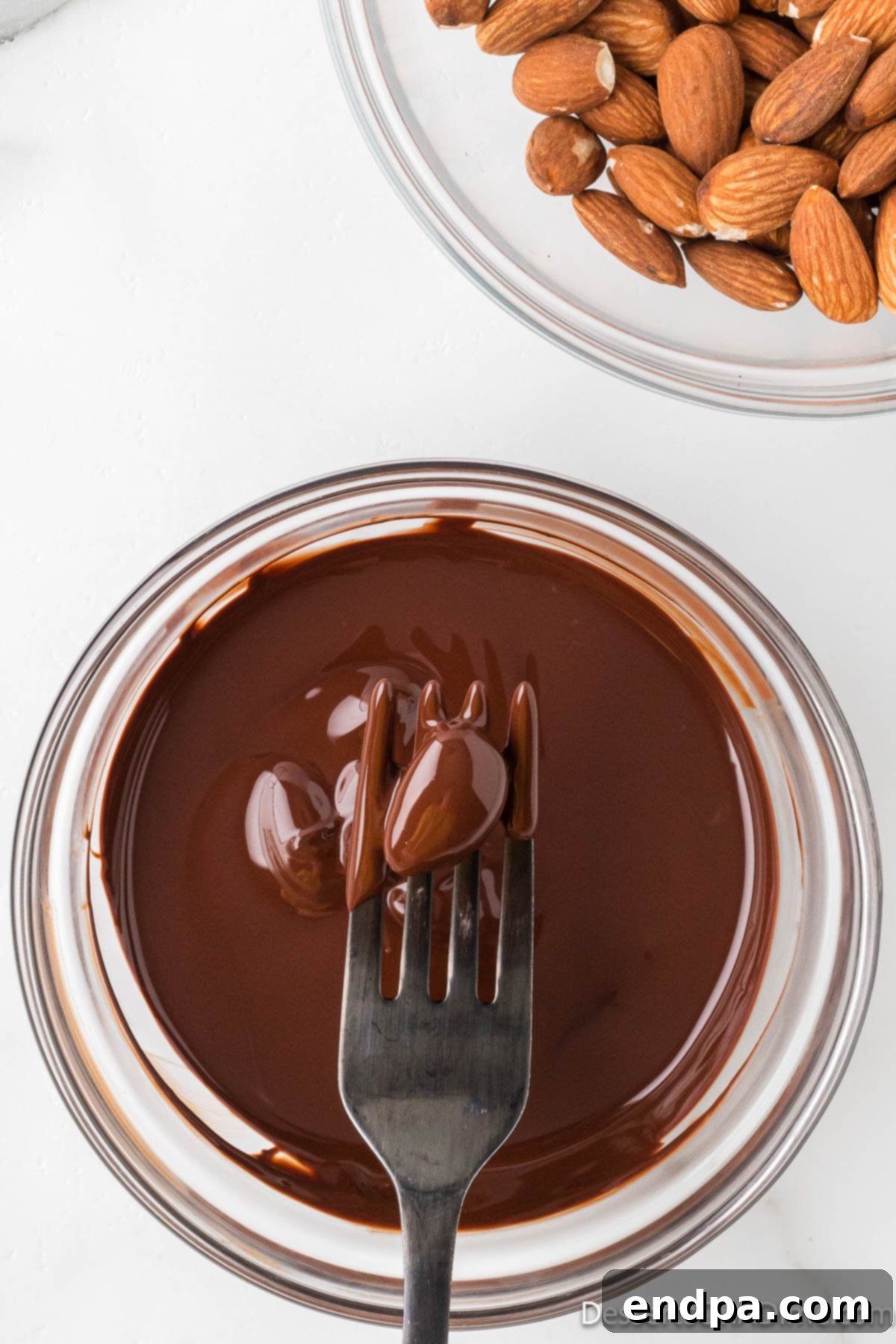 Decadent Dark Chocolate Almonds 6 A fork lifting a chocolate-covered almond, allowing excess chocolate to drip back into the bowl.