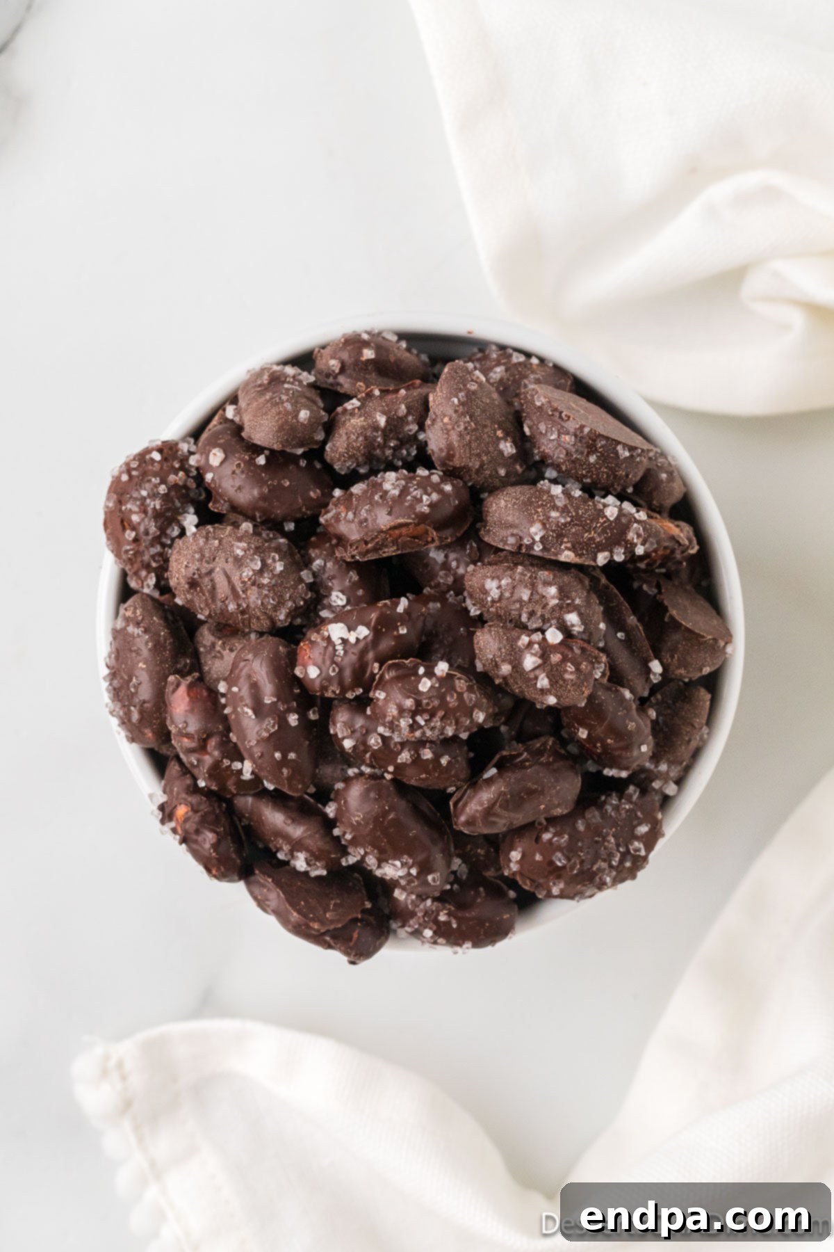 Decadent Dark Chocolate Almonds 9 Close-up of dark chocolate covered almonds in a pristine white bowl, ready to be enjoyed.