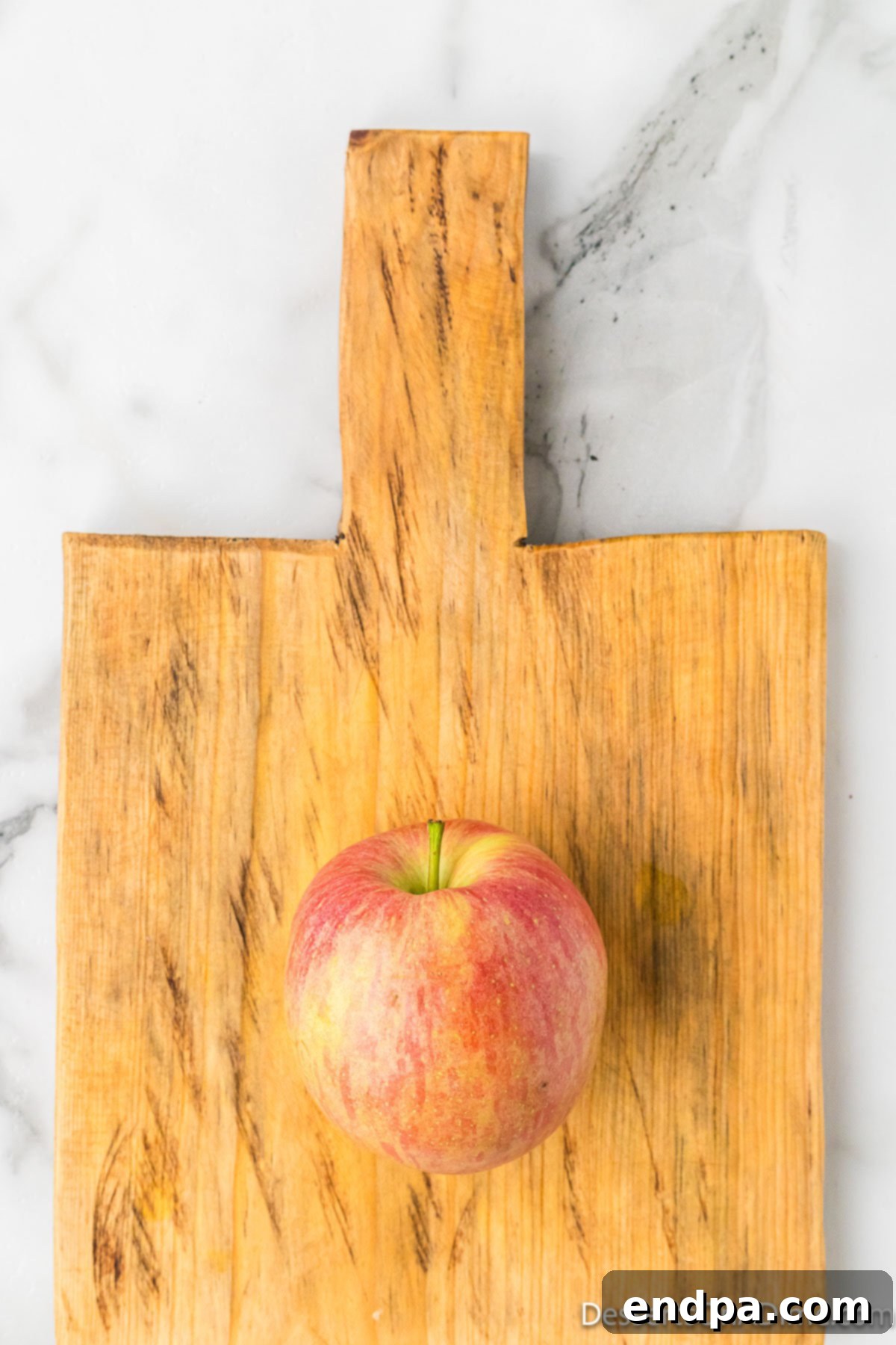 Sweet & Crispy Air Fryer Apple Chips 4 A crisp red apple resting on a clean wooden cutting board, ready for preparation.