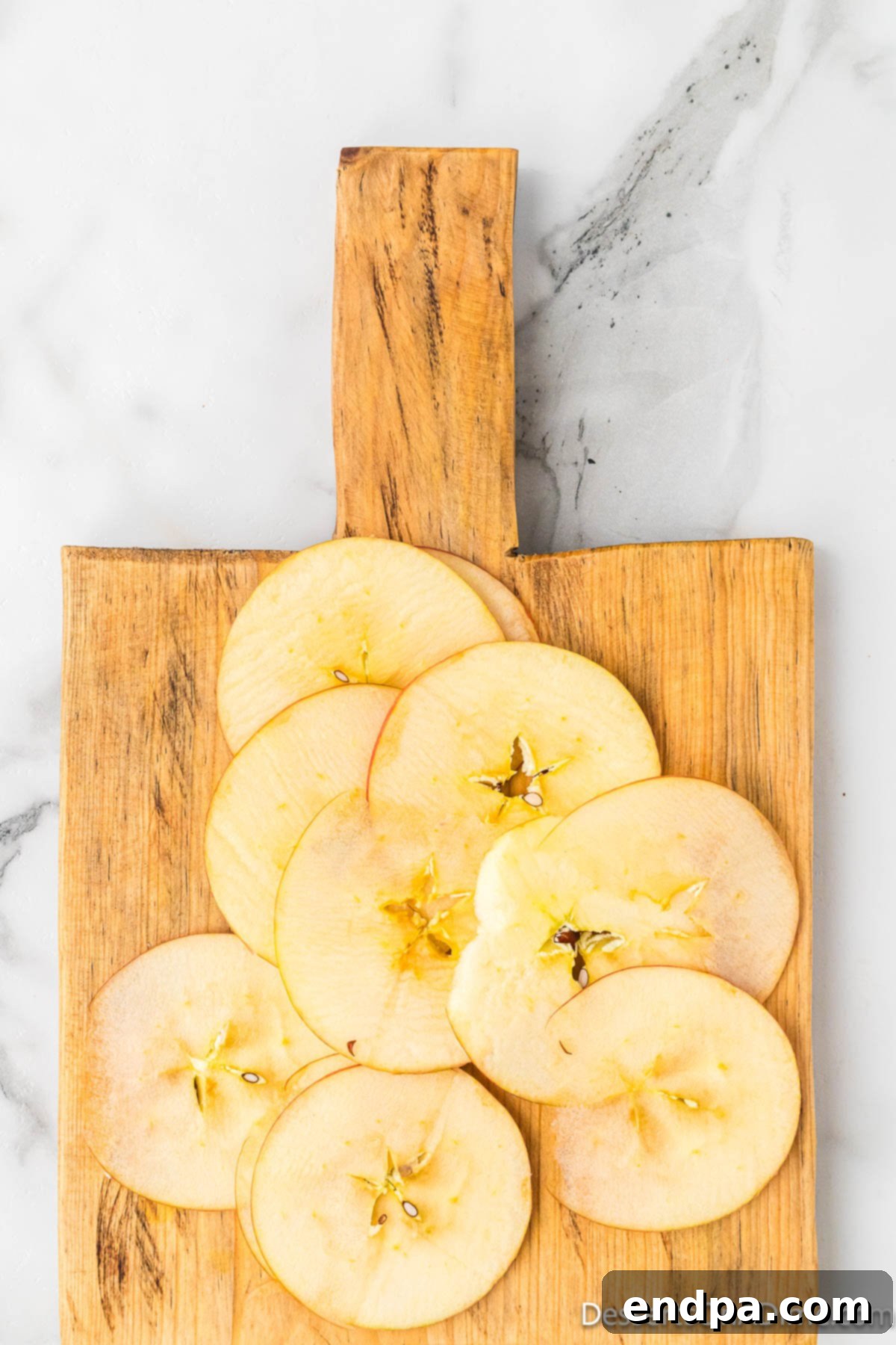 Sweet & Crispy Air Fryer Apple Chips 5 Thinly sliced apple rounds meticulously arranged on a wooden cutting board, showcasing uniform thickness.