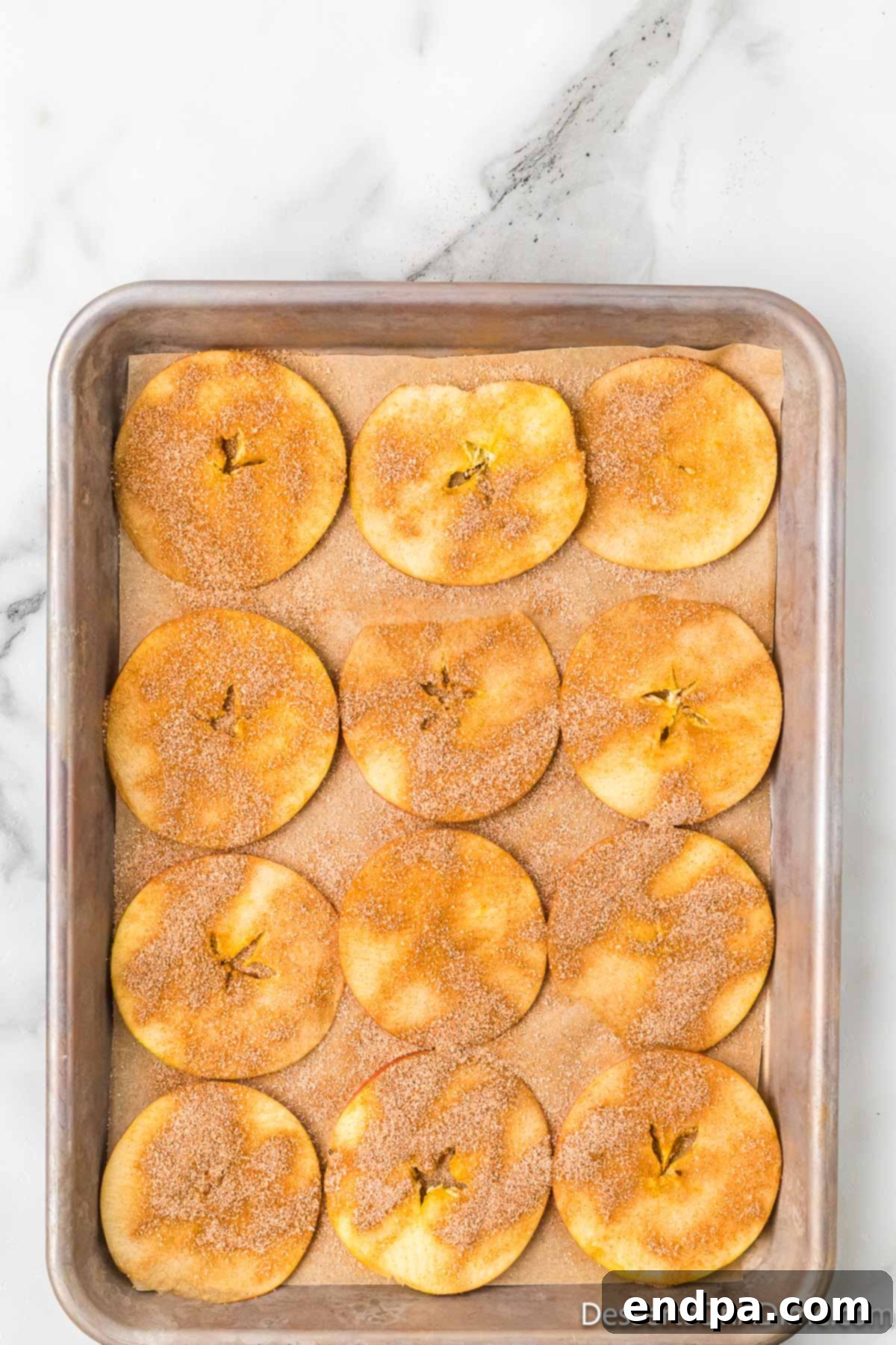 Sweet & Crispy Air Fryer Apple Chips 8 Freshly sprinkled cinnamon and sugar mixture generously coating thin apple slices on a flat surface.