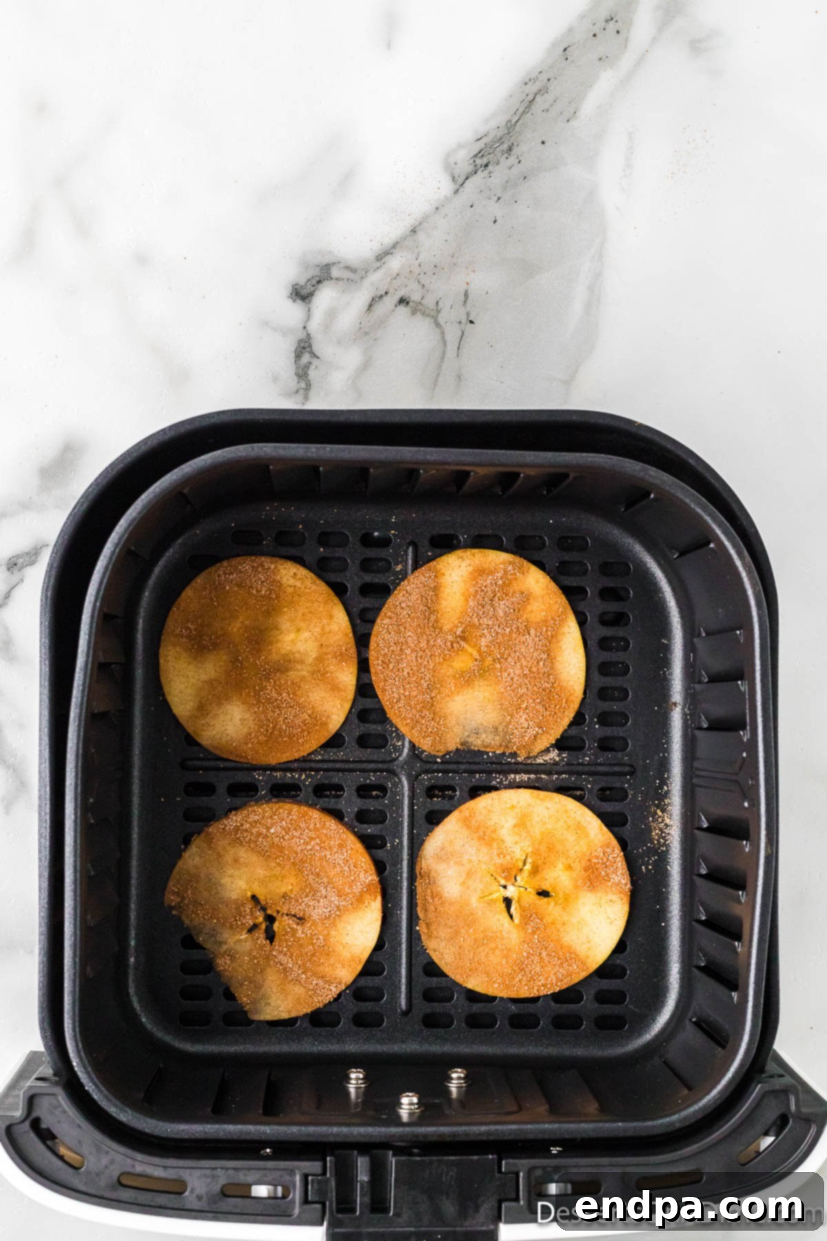 Sweet & Crispy Air Fryer Apple Chips 9 Thin apple slices, coated with spices, carefully arranged in a single layer within an air fryer basket.