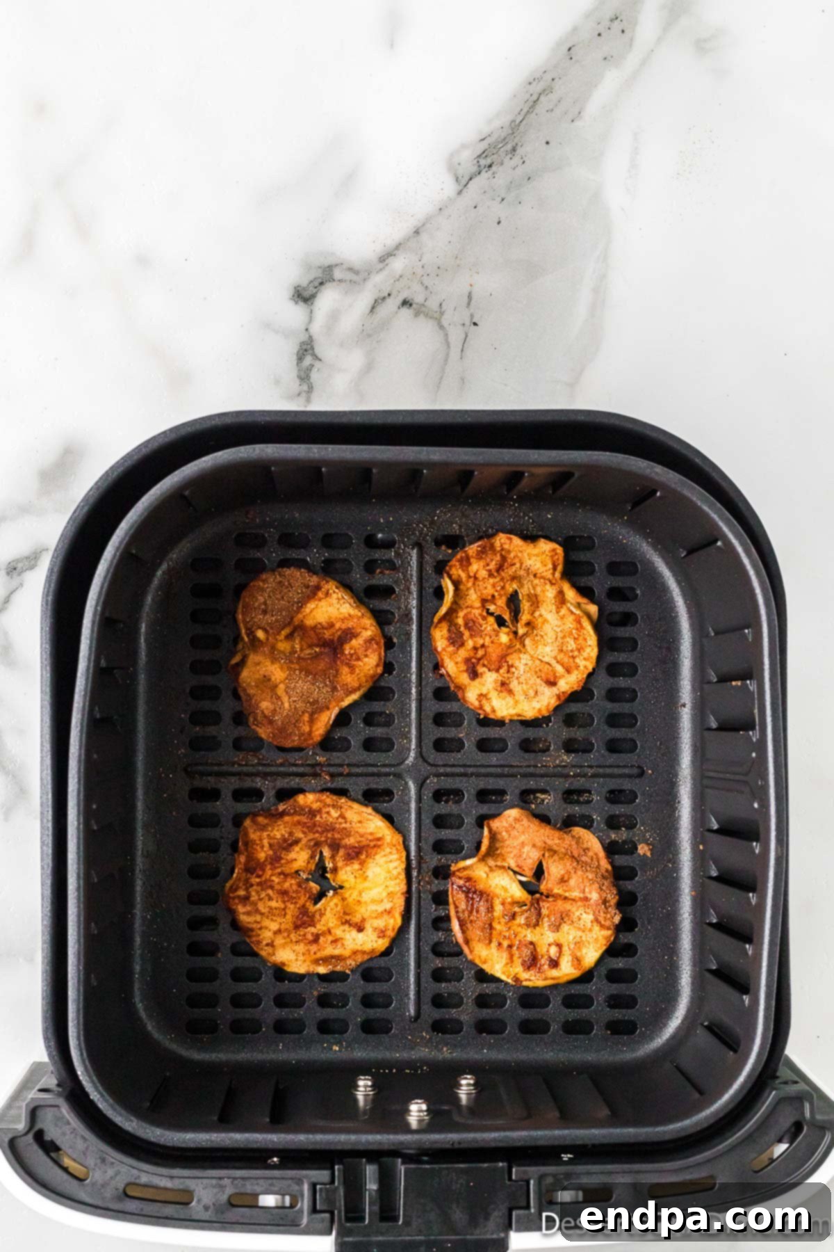 Sweet & Crispy Air Fryer Apple Chips 10 Apple slices nestled inside an air fryer basket, mid-cooking, showing initial signs of golden brown crisping.