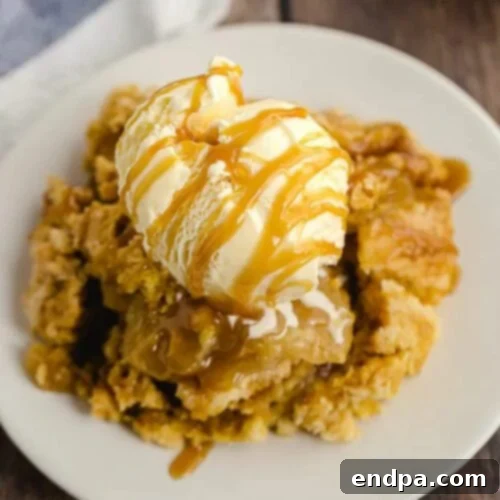 Close up image of caramel apple dump cake on a white plate topped with ice cream and caramel sauce.